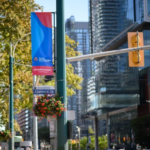 A street sign for Clarence Square and a banner for the Toronto Downtown West Entertainment District on a city pole.
