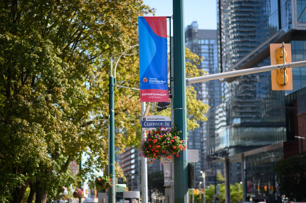 A street sign for Clarence Square and a banner for the Toronto Downtown West Entertainment District on a city pole.