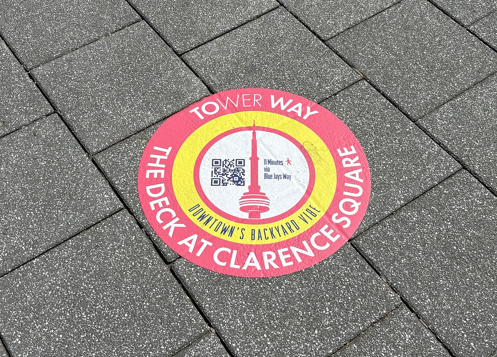 Circular sidewalk decal for The Deck at Clarence Square, featuring an illustration of the CN Tower and a QR code.