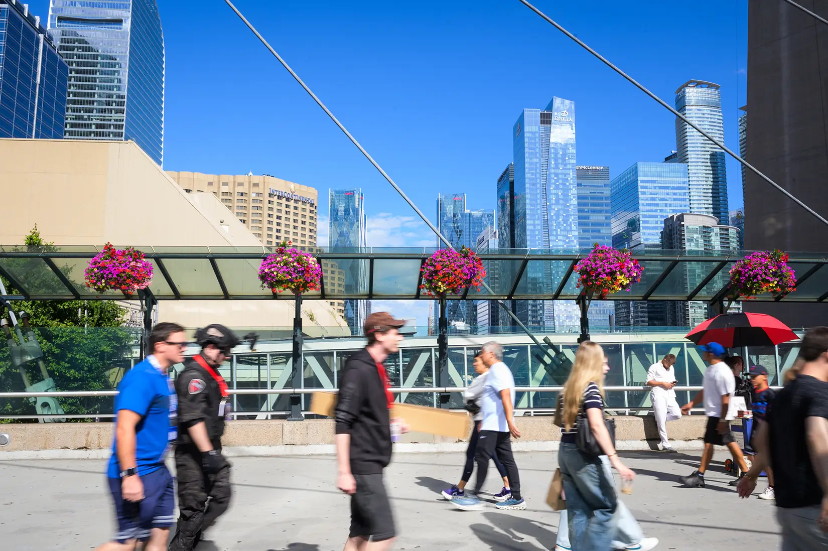 People walking on an elevated city walkway with a skyline of glass skyscrapers in the background.