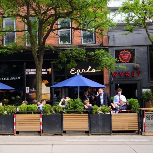 Outdoor patio seating at Earls and WVRST restaurants, with people dining under blue umbrellas.