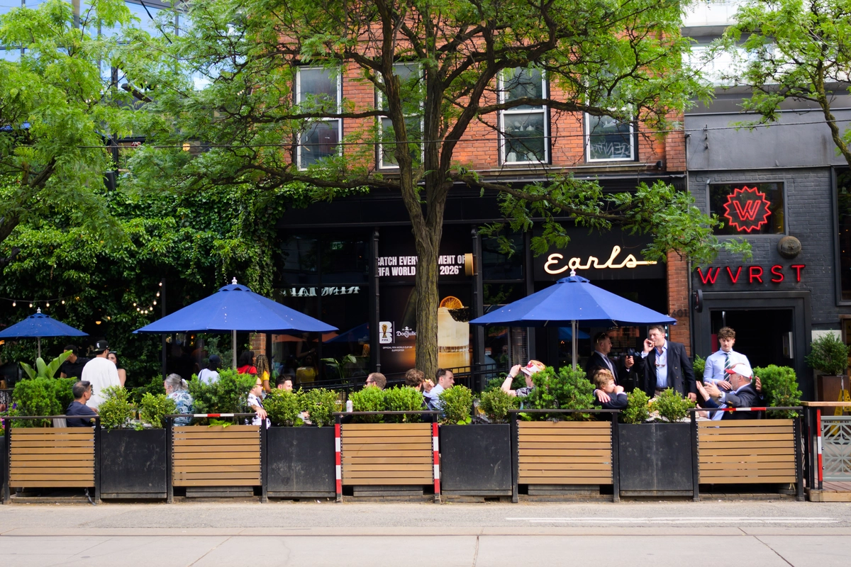 Outdoor patio seating at Earls and WVRST restaurants, with people dining under blue umbrellas.