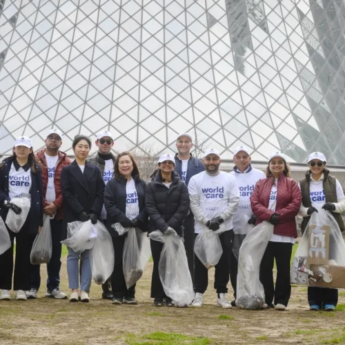 A group of volunteers wearing white World of Care caps and shirts posing with bags of collected trash.