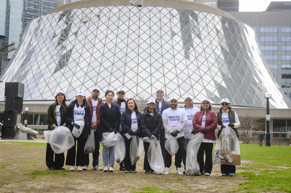 A group of volunteers wearing white World of Care caps and shirts posing with bags of collected trash.