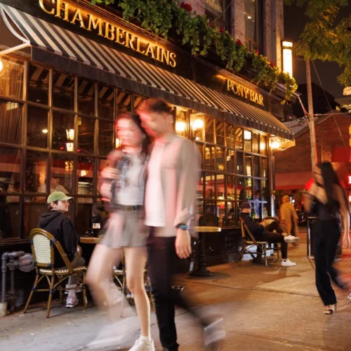 People walking on a sidewalk past the entrance to Chamberlains restaurant at night.