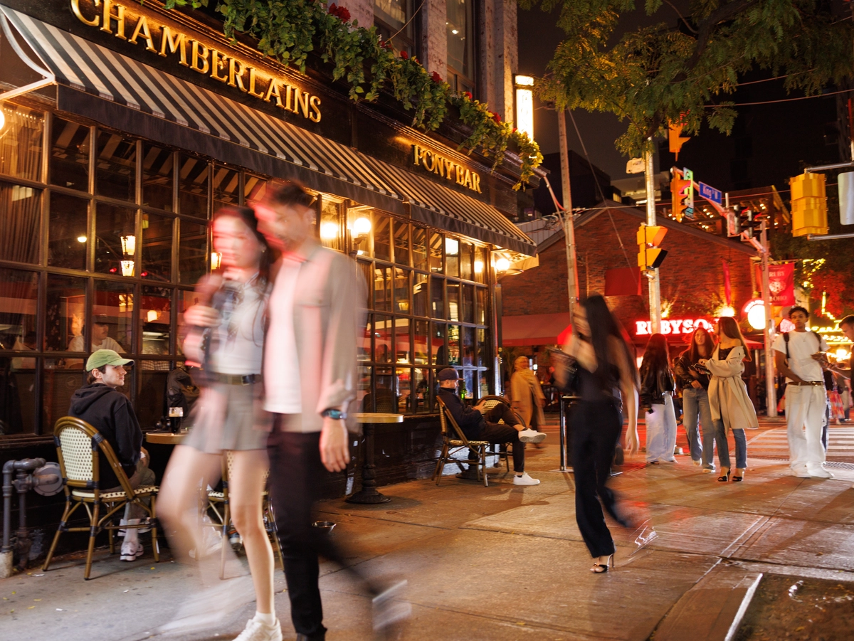 People walking on a sidewalk past the entrance to Chamberlains restaurant at night.