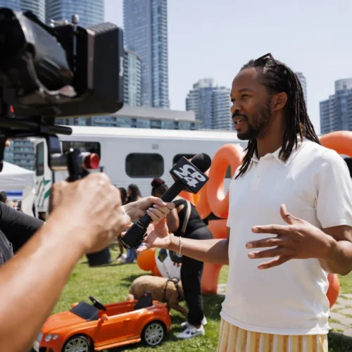 A reporter holds a CP24 microphone toward a man being interviewed outdoors in front of a city skyline.