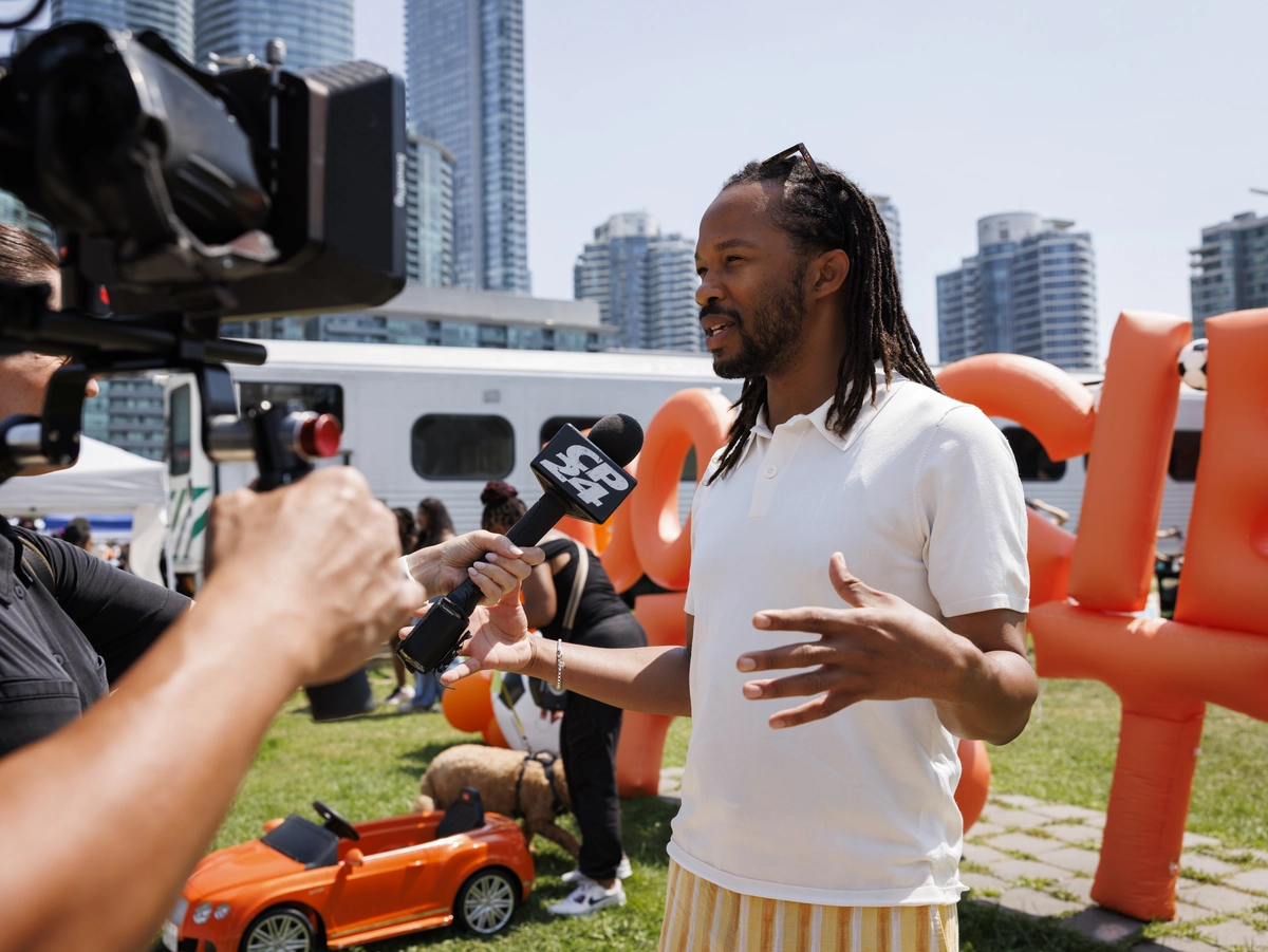 A reporter holds a CP24 microphone toward a man being interviewed outdoors in front of a city skyline