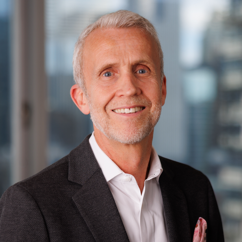A smiling middle-aged man with gray hair wearing a dark blazer and white dress shirt.
