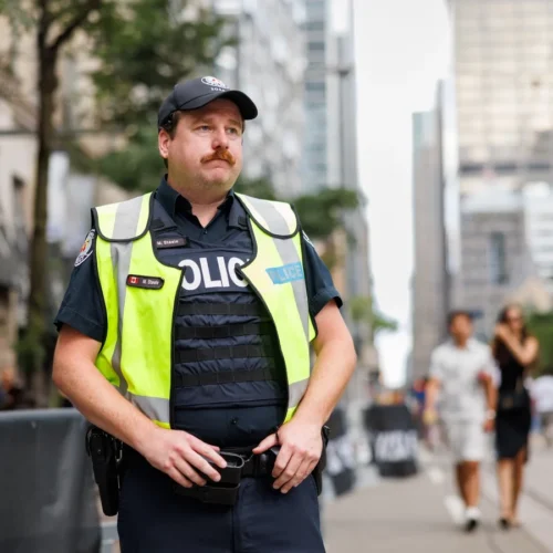 A police officer in a high-visibility vest stands on a city street.