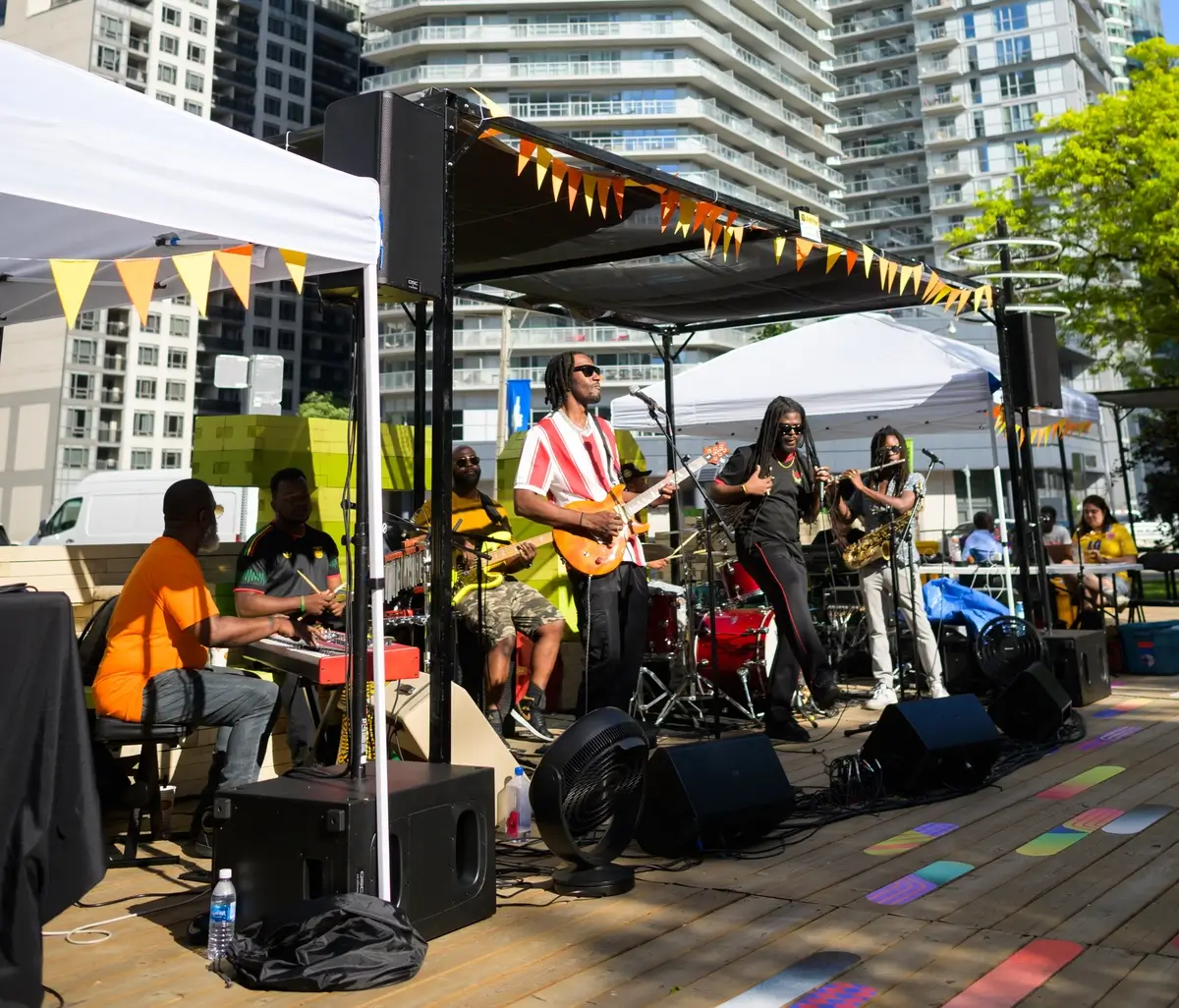 A live band plays on an outdoor stage with urban buildings in the background.