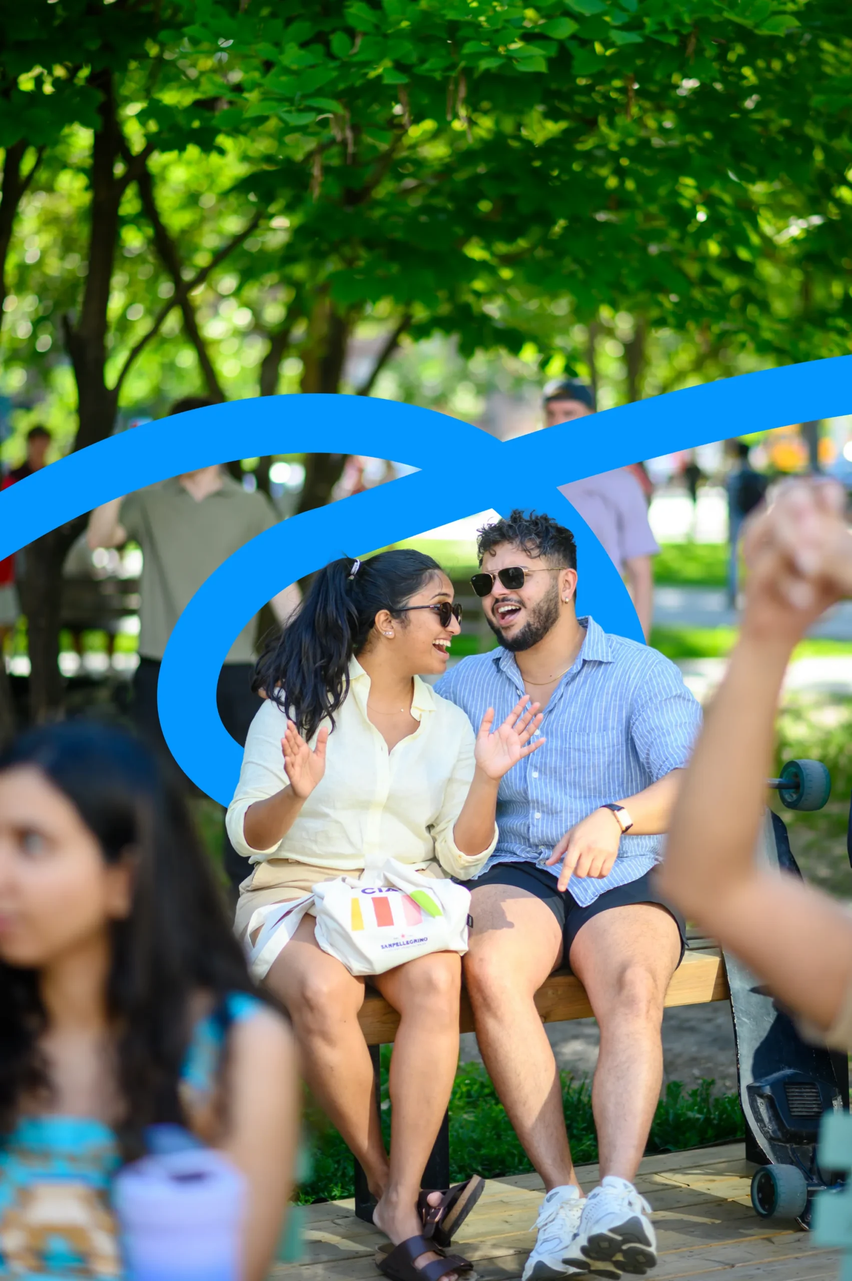 A man and a woman in sunglasses sitting on a bench in a park, laughing and talking.