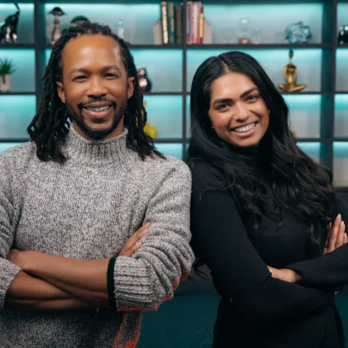 A man with dreadlocks and a woman with long dark hair smiling side-by-side with arms crossed.
