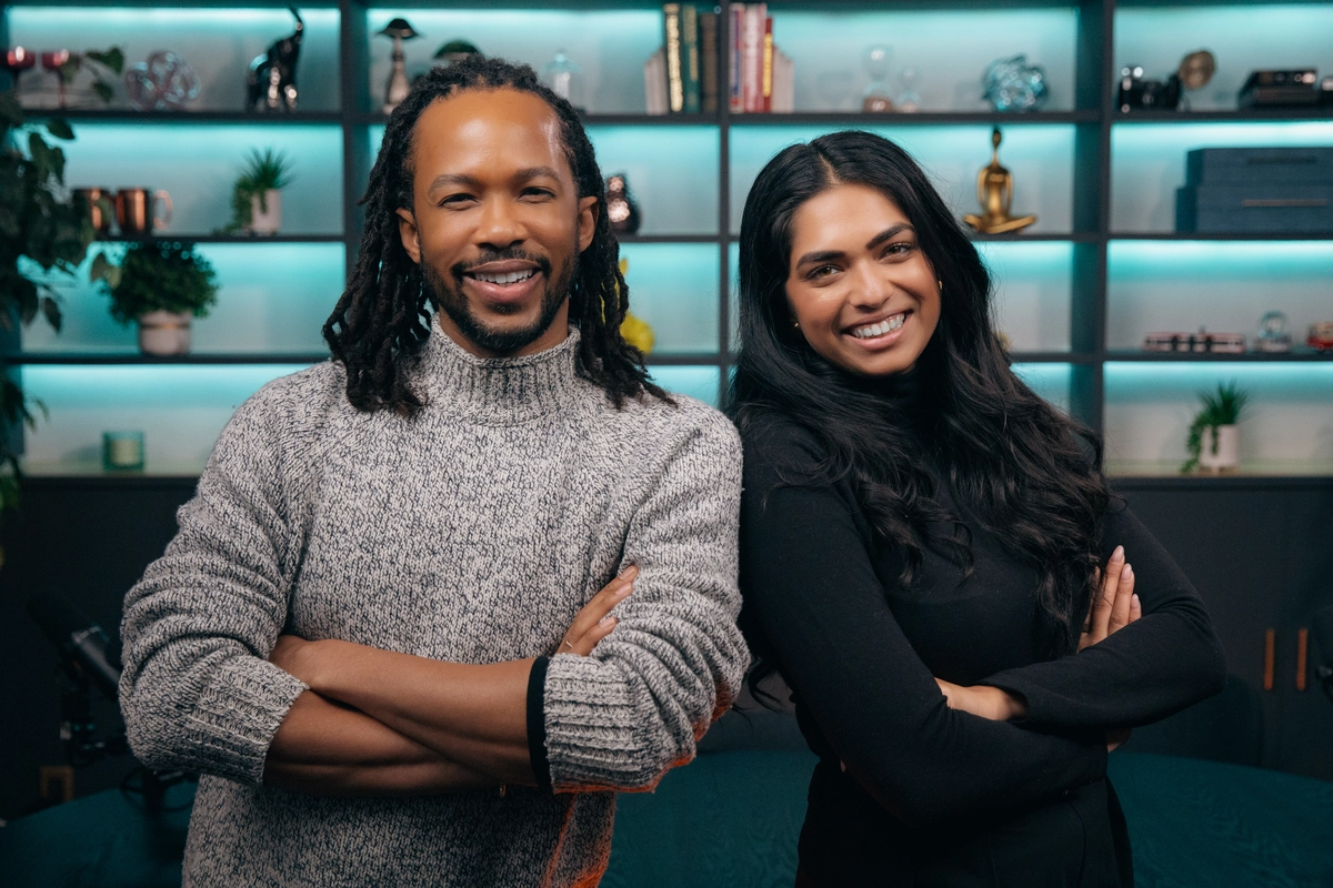A man with dreadlocks and a woman with long dark hair smiling side-by-side with arms crossed.