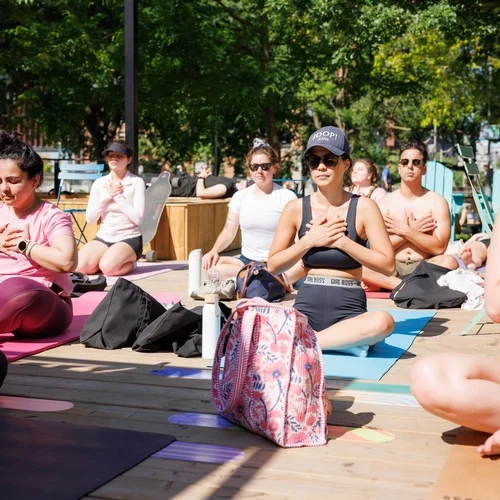 A group of people sitting on yoga mats on a wooden deck with their hands over their chests.