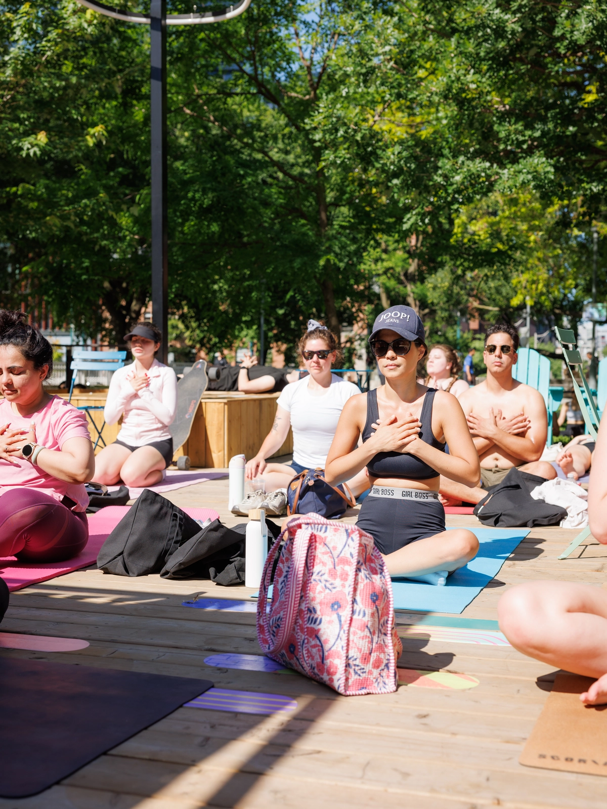 A group of people sitting on yoga mats on a wooden deck with their hands over their chests.